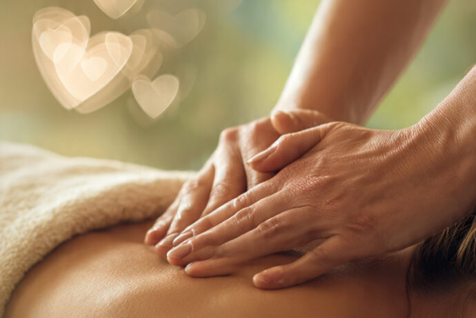 Hands gently massaging a back with soft lighting, subtle heart shapes, and green leaves, symbolizing February self-care and heart health.